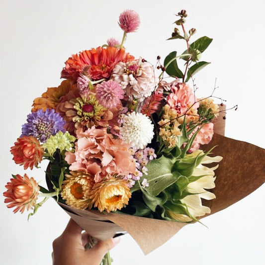 Bouquet of colorful flowers held by a hand against a white background