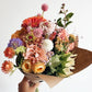 Bouquet of colorful flowers held by a hand against a white background